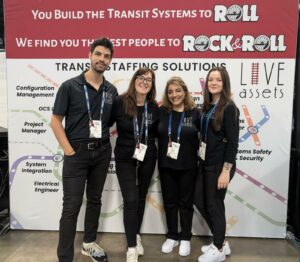 Live Assets staff looking cheerful standing in front of red and white promotional poster. 